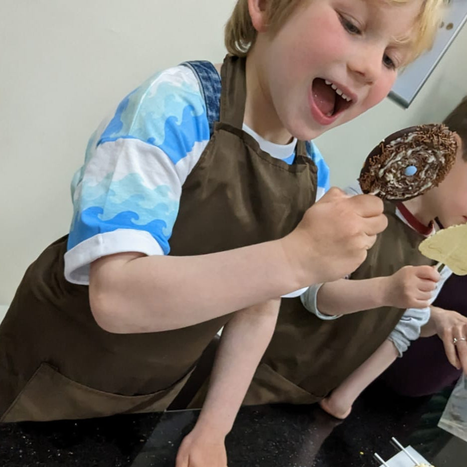 Children in a kitchen setting with one child holding a chocolate lolly